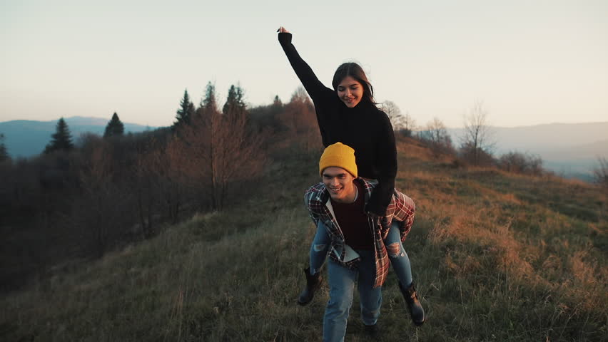 Young couple in love on vacations enjoying mountains. Attractive man is carrying girlfriend on his shoulders and whirls her. Having fun