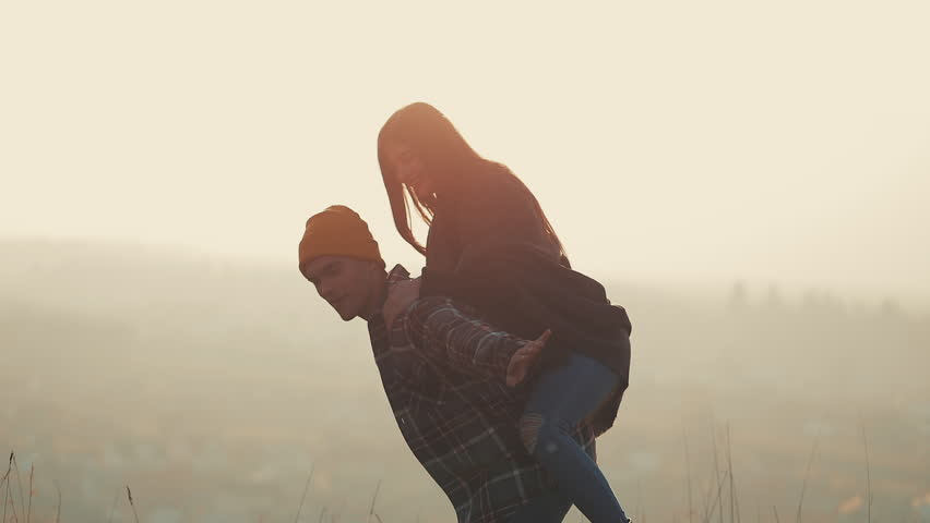 Young couple in love on vacations enjoying mountains. Attractive man is carrying girlfriend on his shoulders and whirls her. Having fun