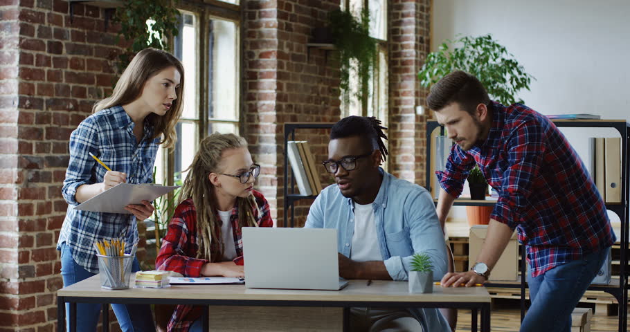 Multiethnical group of students brainstorming for their studing project at the college at the laptop computer and talking about an exam. Indoors.