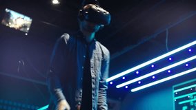 Young Man Wearing Virtual Reality Headset and Holding Controllers Plays in a Video Game