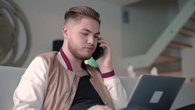 Confident freelancer answering customer question on phone. Young guy in casual sitting on couch with laptop, typing and speaking on cell, saying no. Consulting or multitasking concept