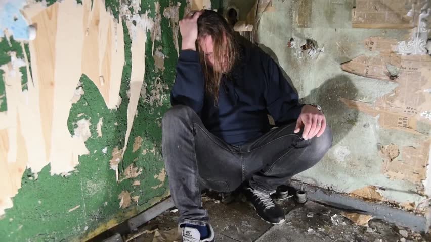 Depressed and angry man is sitting in the corner in an abandoned house