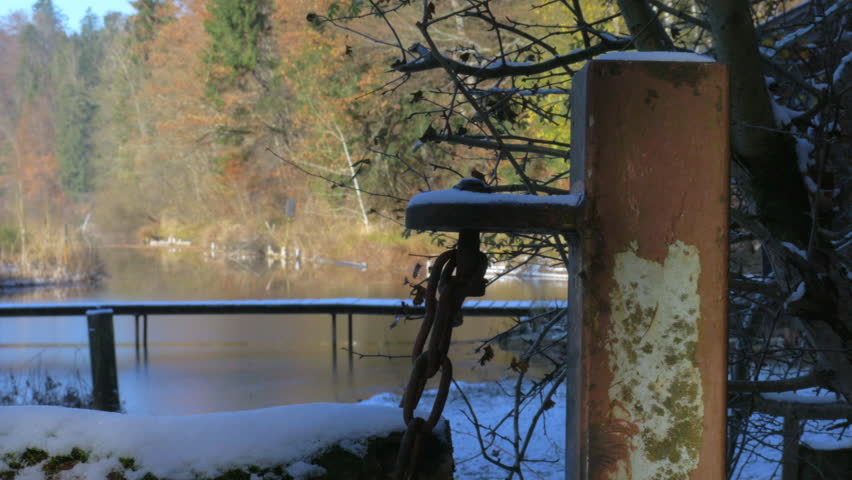 First autumn snow at a lake in Bavarian forest, trees still covered in fall foliage colors, narrow footbridges leading across the water. Solitude and tranqulity, outdoors hiking in cold sunny weather