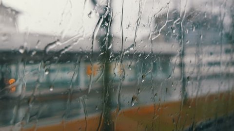 Close-up shot of rain drops and streaks on the window od moving bus by the city street in deep autumn