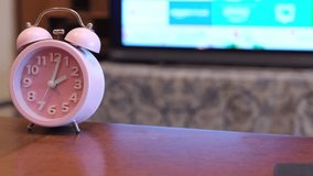 Pink alarm clock on coffee table in front of television set. Panning to the right.