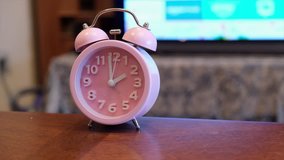 Pink alarm clock on coffee table in front of television set. Tracking footage.