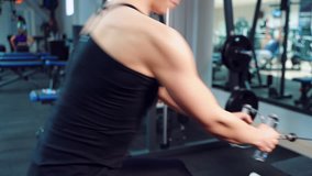 A woman in a black top performs an exercise for pumping the press and biceps against the background of sports equipment in a fitness club. Close-up