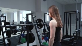 Slender woman in sportswear comes to the weight bar and lifts it in the gym near the mirror. Healthy lifestyle
