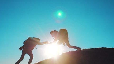 lifestyle teamwork people tourists business travel trip lends a helping hand. two men with backpacks hiking help each other silhouette in mountains with sunlight. slow motion video. teamwork