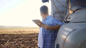 smart farming driver . man farmer driver stands with a digital lifestyle tablet near the truck. slow motion video. Portrait businessman farmer standing in the field harvesting season car. driver