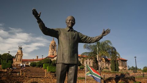 Pretoria, South Africa - circa January 2019: Nelson Mandela statue at the  sandstone Union Buildings, government offices, with South African flag flying in background on sunny day, dolly move forward
