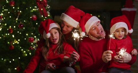 The slow motion of happy cheerful family wearing santa hat singing a Christmas Song with sparklers in their hands. Shot with RED camera in 8K. Concept of Christmas time, winter holidays, family fun.