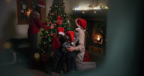 Slow motion of happy family having fun to celebrate Christmas holidays, opening presents view from snowy window. Shot with RED camera in 8K. Concept of Christmas time, winter holidays,family tradition