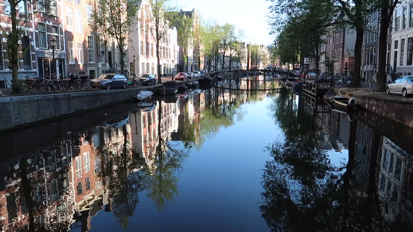 Beautiful cityscape of Amsterdam at sunny day with a canal and houses on its side with a bridge at background. Amsterdam Netherlands. Flat plane