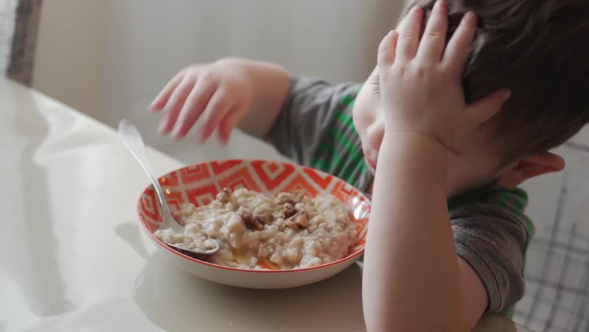 Cute little baby alone eats porridge with a spoon from a plate, the concept of healthy eating.