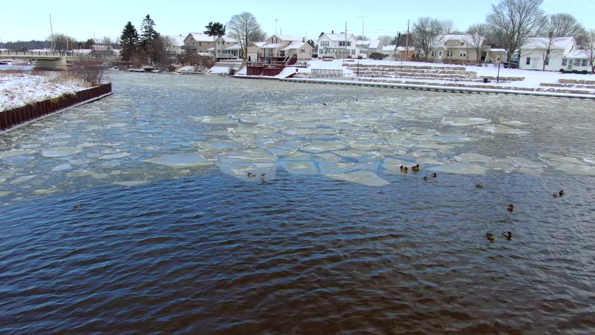 Very icy river in scenic Small town, with bridge, fishing boats.
