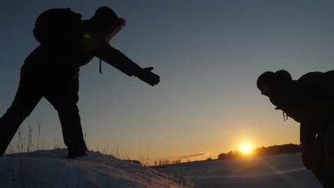 Men help each other to conquer the summit of high snowy mountain by holding hands and stretching each other to top at sunset. Cold natural conditions when traveling. Extreme hikes for brave.
