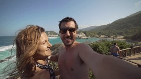 happy couple taking selfie photo in front of the sea in Tayrona National Park, Tropical Colombia. Crazy tourists travelling on the white beach of caribbean sea. 4K video
