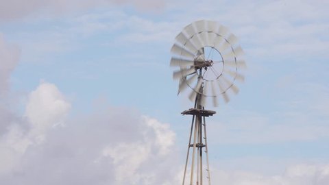 Close-up 4K shot of an old rustic farm windmill blowing and spinning in the wind with a partly cloudy blue sky in the
background.