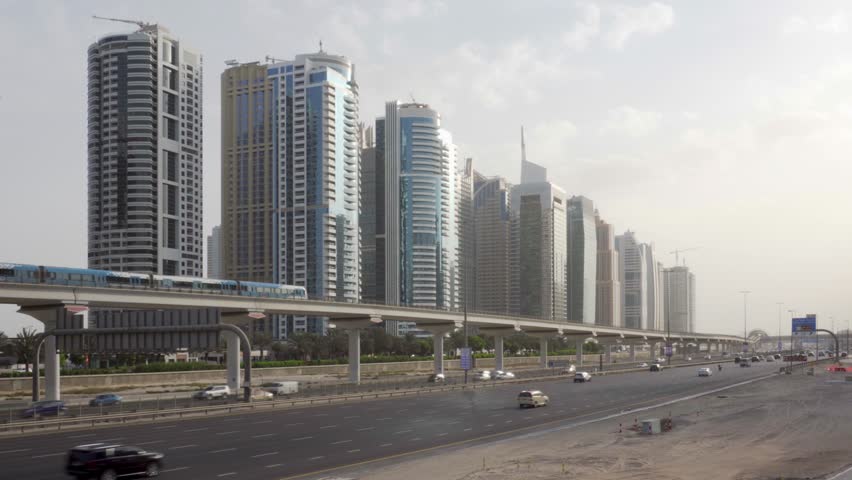 Train of the Dubai Metro passing above Sheikh Zayed Road in Dubai, United Arab Emirates (UAE). Amazing view of the highway and elevated viaduct of the Red Line on high-rise buildings background.