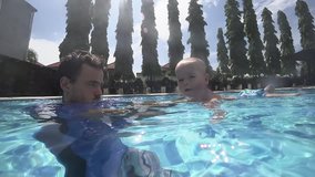 Happy smiling toddler is diving under water with father in the swimming pool. Priceless health care for your baby. An underwater slowmotion video. Important to spend enough time with your kids