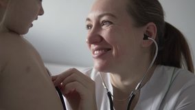 Beautiful doctor listens to the heartbeat of the child. A woman in a white coat, puts a stethoscope to the breast of a child, smiles and listens to a little girl. A child in a hospital ward. Close-up - Powered by Shutterstock - Get 15% off with code: PIKWIZARD15