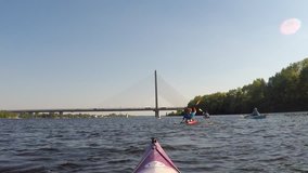A group of kayakers sailing on the river/lake towards a bridge, on a bright sunny day. 
Video shot from the first point of view on one of the kayakers. 
No identifiable people. 