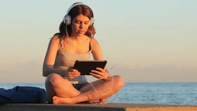 Concentrated teen browsing and listening media on a tablet at sunset on the beach