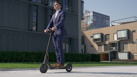 Slow motion - Adult male in business attire riding with electric scooter to work