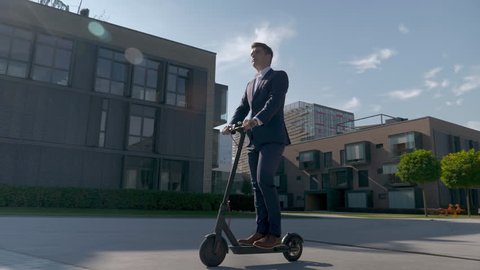 Slow motion - Adult businessman riding with electric scooter to work