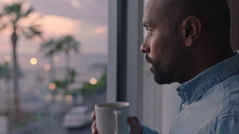 attractive man drinking coffee looking out window in hotel room enjoying early morning view at sunrise contemplating future planning ahead