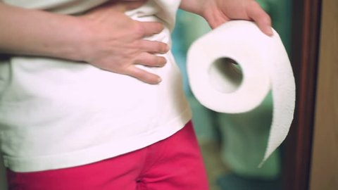A woman with toilet paper holds on to a sore stomach, goes to the toilet. 