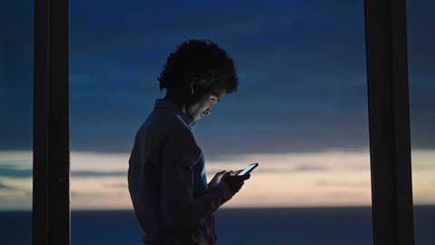 young man using smartphone in hotel room texting sharing vacation lifestyle on social media enjoying view of ocean at sunset