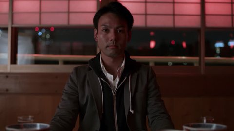 Portrait of a Japanese man sitting at a table inside of a cruise ship with soft interior lighting at night. Medium to close up shot on 4k RED camera.