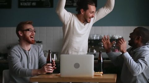 Diverse male friends hangout in pub drink beer watching online football game match at laptop, men fans buddies supporters cheering celebrating victory goal score support winning team, sport betting