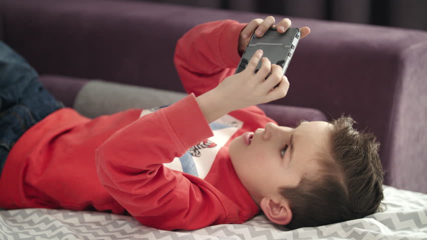 Boy playing mobile game on smartphone on sofa. Preschooler playing mobile phone. Kid using phone for gaming. Child playing video game at home