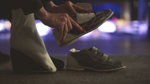The girl puts her bowling shoes on before playing bowling in a bowling club. Beautiful manicured woman’s hands with red nail polish. Young woman holding a bowling shoe. Close up