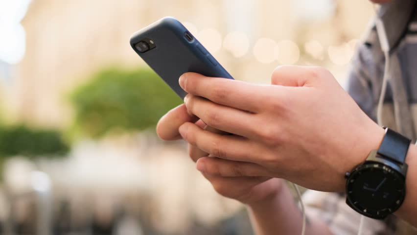Young man using smartphone scrolls through social media feed on device, checking mail, reading news on app. 
