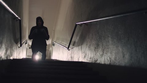A hooded male fighter descends from a dark stairwell and shadow boxes towards the camera