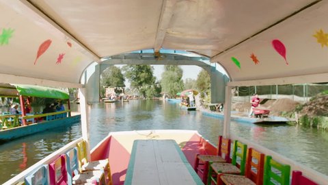 Mexico City / Mexico - December 28 2018: Xochimilco in Mexico City. Bright Colorful Boats Called Trajineras Float Down Mexican River. Camera Moves From Inside Boat to Reveal River and Other People
