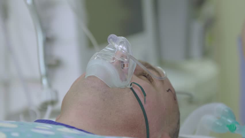 Youg man patient close-up lying in an operating room with an oxygen mask on his face before the surgery (4k, 25fps)