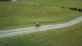 Aerial View bicyclist rides on a mountain road in summer sunny day around trees and mountains background under sun light, Drone 4K Video Aerial View
