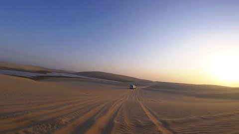Smooth first person video of following a car over sand dunes in the desert, sunset time