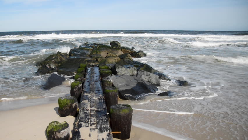 Ocean waves crash into a rock and wooden jetty.