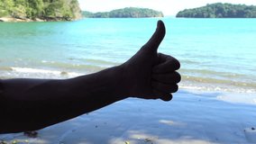 Point of view video shot of white female hand forming ok gesture with thumb up at sunny blue sky and sea background. Perfect beach holiday concept.