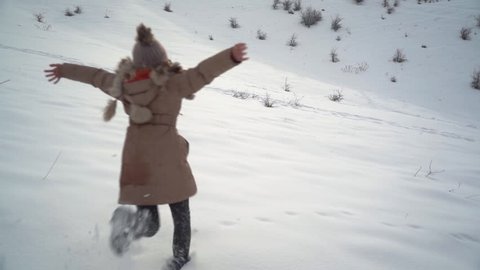Young beautiful girl runs on the snow and jumps into it and starts making a snow angel. Slow motion video 100p