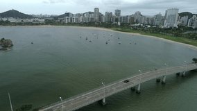 Drone aerial zoom in on Brazilian beach landscape. In the background buildings and constructions. Boats docked near the beach. Cloudy Sky. Video Recorded in Vitória, Espirito Santo. 