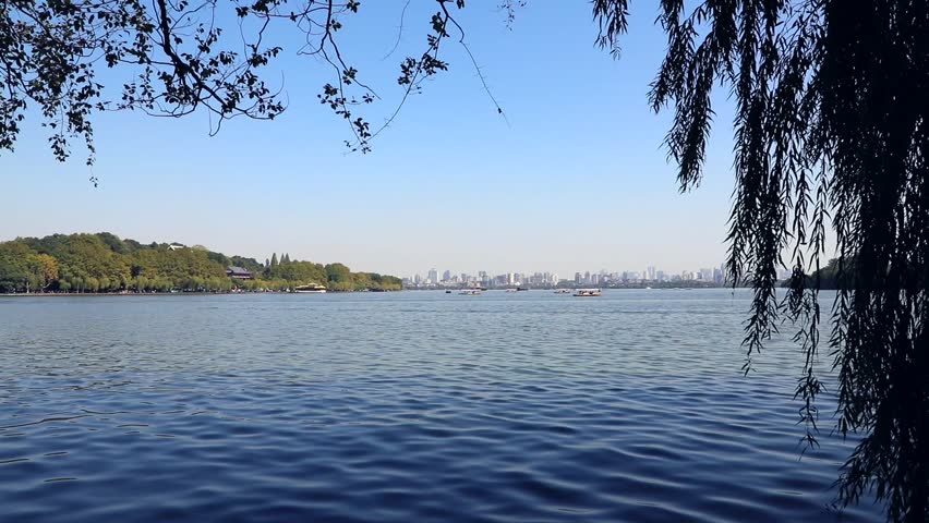 Small Chinese fishing boat with boatman goes to the West Lake coast. Famous park in Hangzhou city center, China 