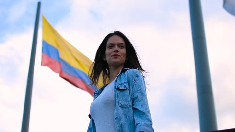 Slow motion of the beautiful young girl and Colombian flag in wind, Happy tourist young woman posing in front of national flag of Colombia