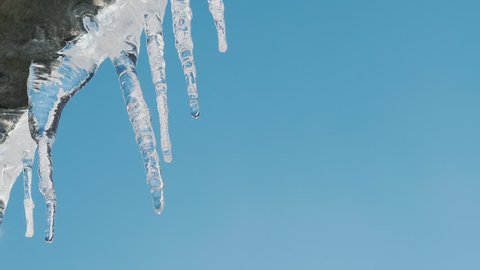 Icicles on the roof melt in the sun against the blue sky. Closeup slow motion video